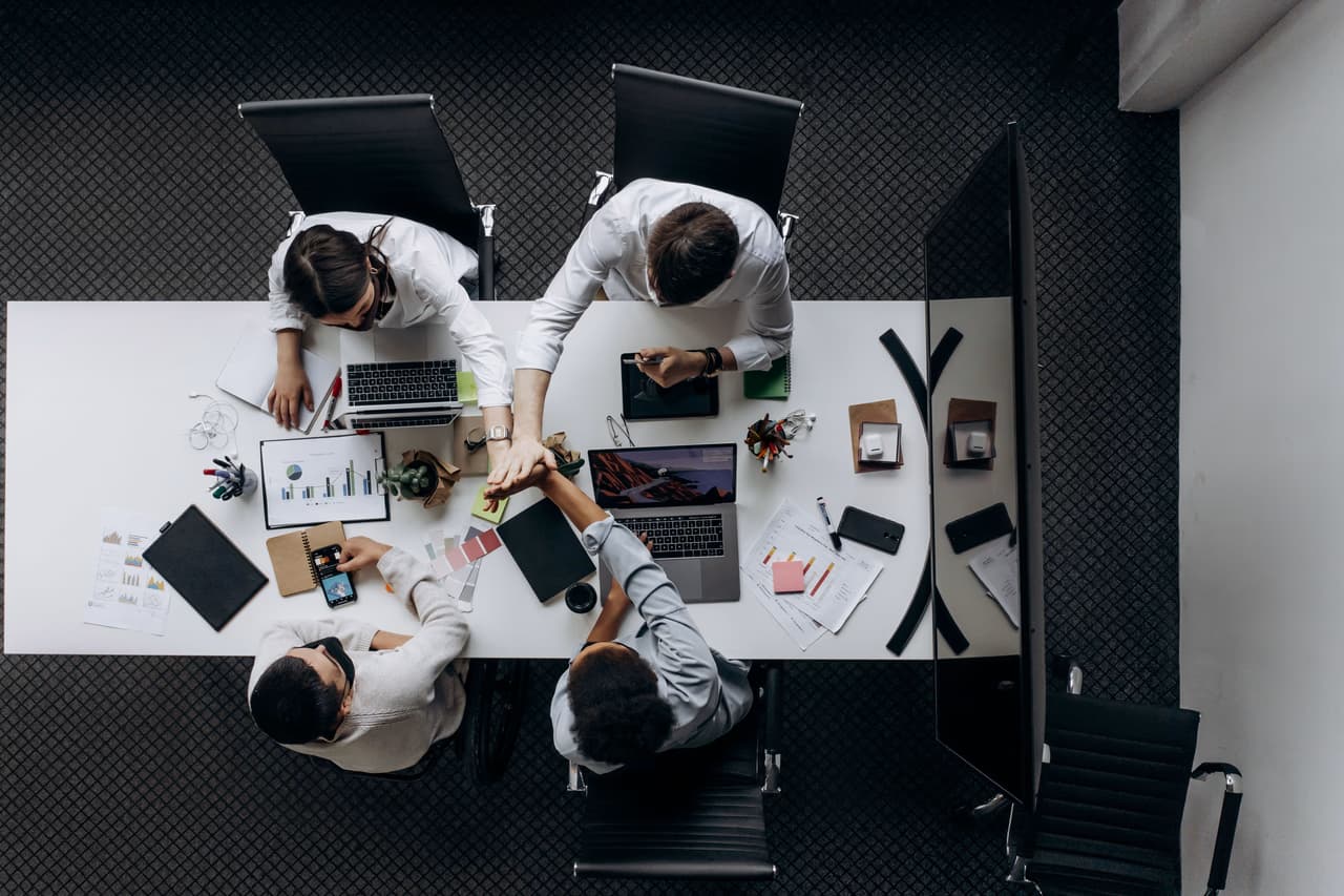 Overhead view of four colleagues working with laptops around a long desk