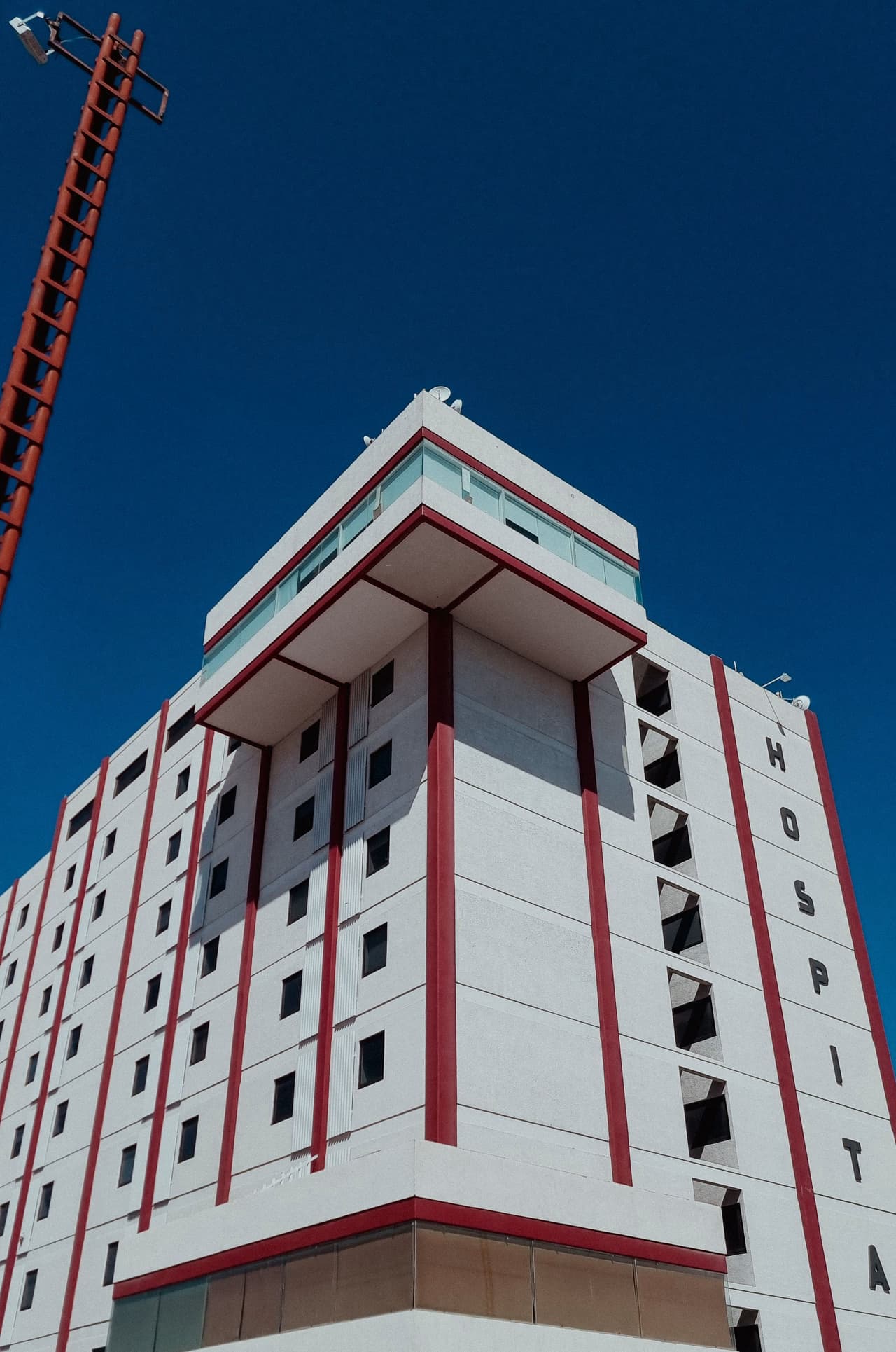 A white and red multi-storey hospital building against a clear blue sky